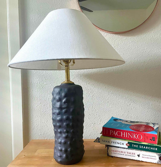 Wheel-thrown lamp by hey moon ceramics, using black clay. bumps created by hand-manipulation. Comes with linen coolie style shade and brass hardware professionally wired.