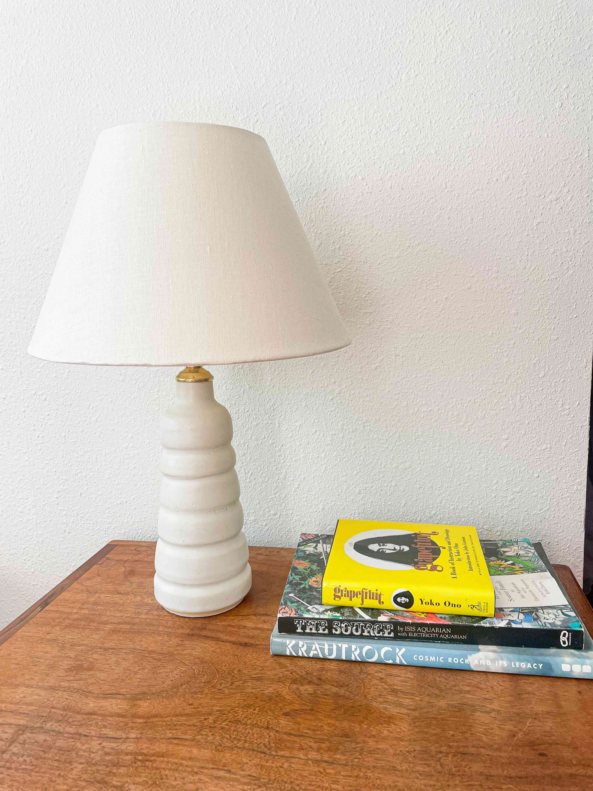 Wheel-thrown ribbed lamp with matte off-white glaze. Made by Hey Moon Ceramics. Comes with linen coolie style shade. Has brass finishes