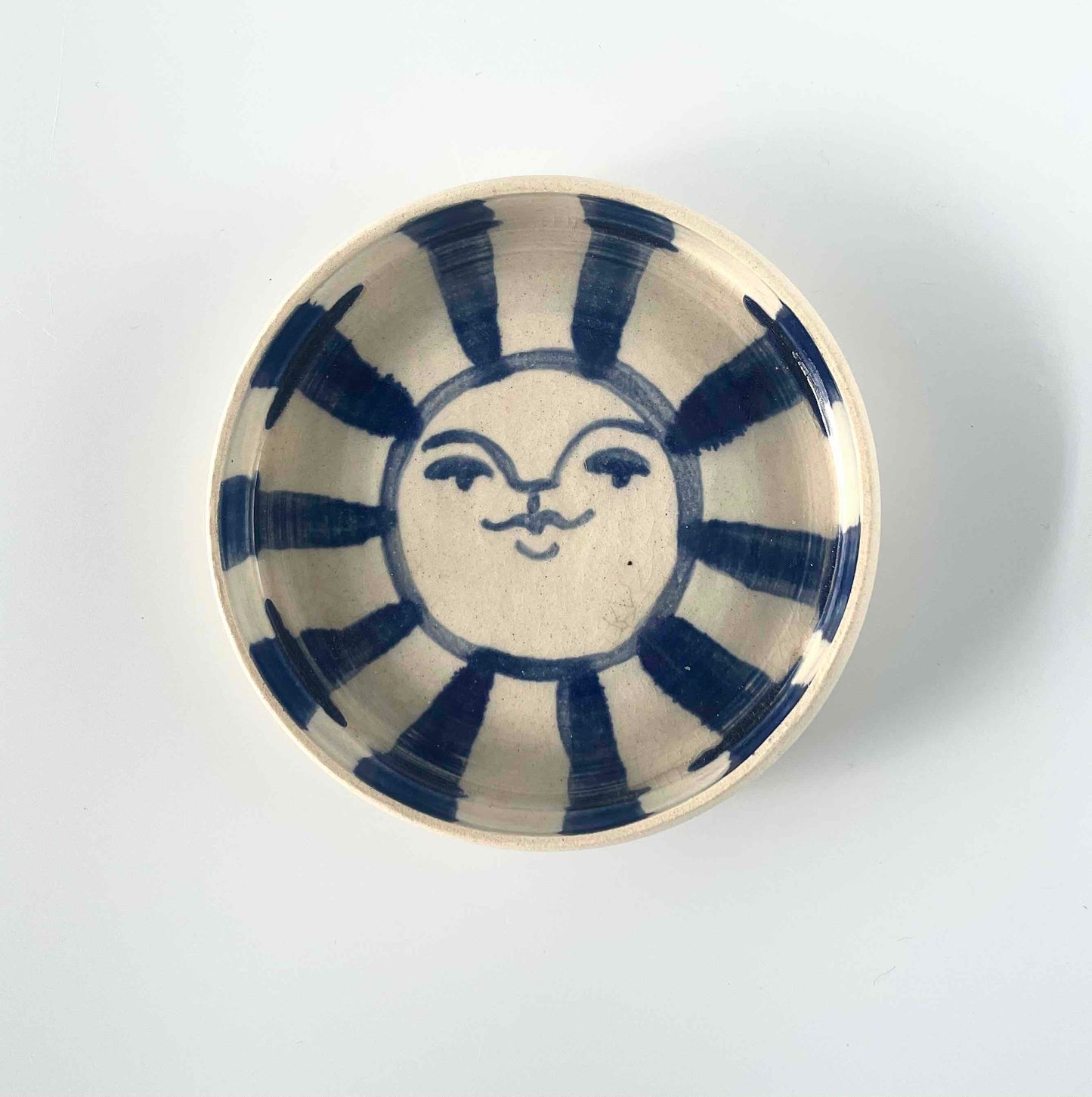 white stoneware catch-all, wheel-thrown by hey moon ceramics. Hand painted with a blue sun face on the interior.